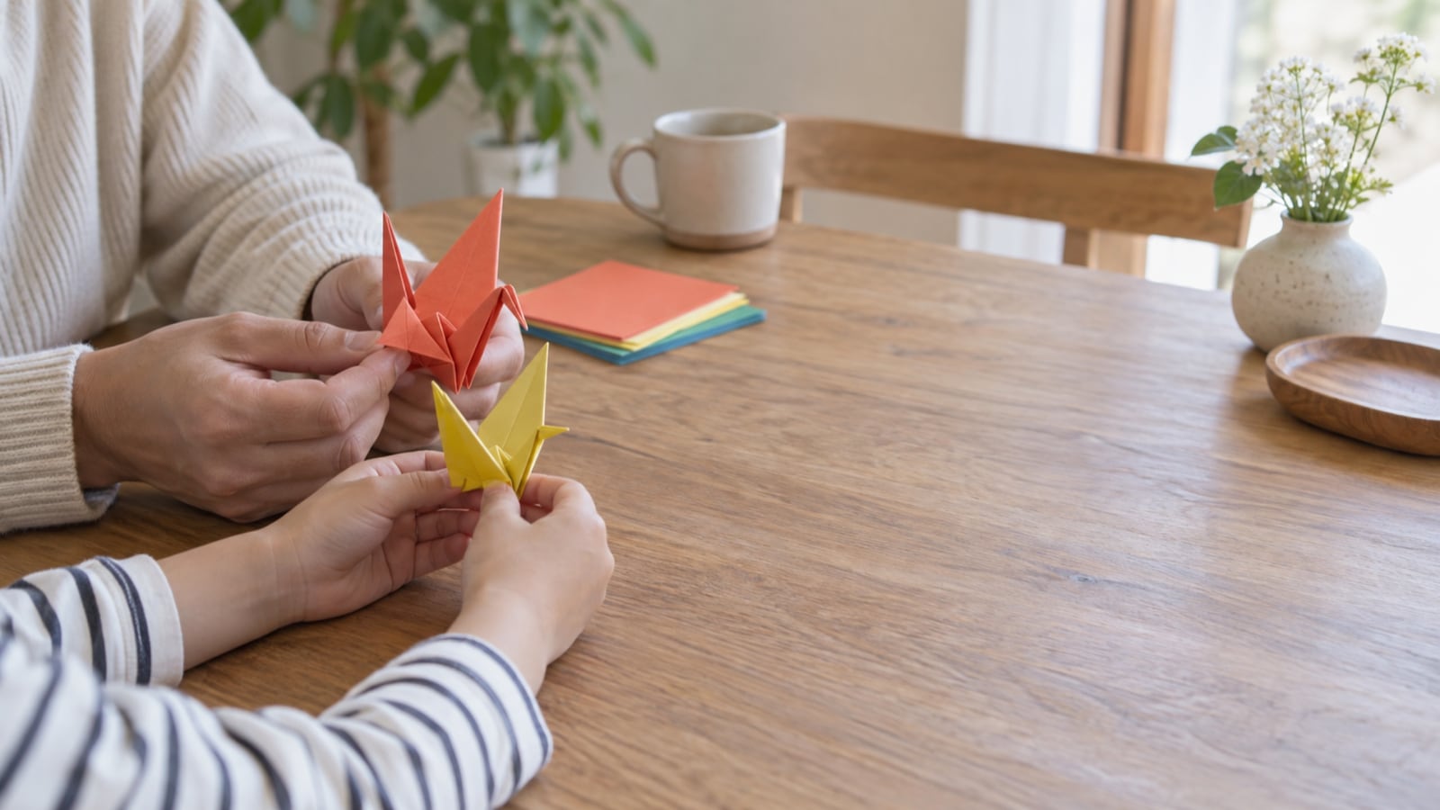 自宅の机で親と子が顔を見せず折り紙の形を比べる