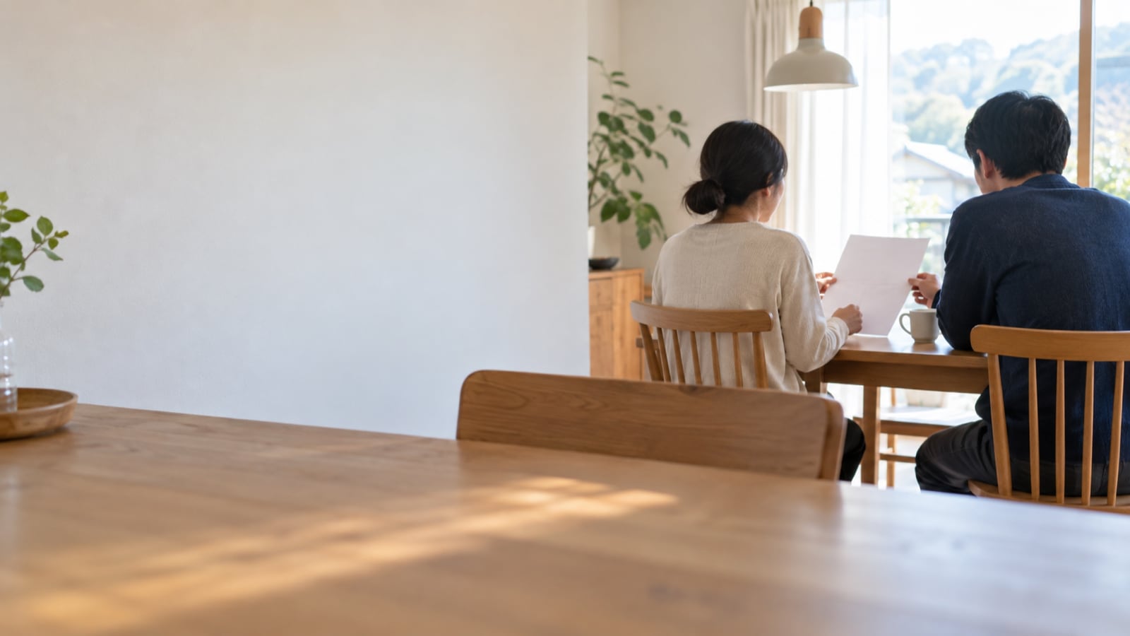 地方の家の食卓で二人の大人が無地の紙を見ながら話す
